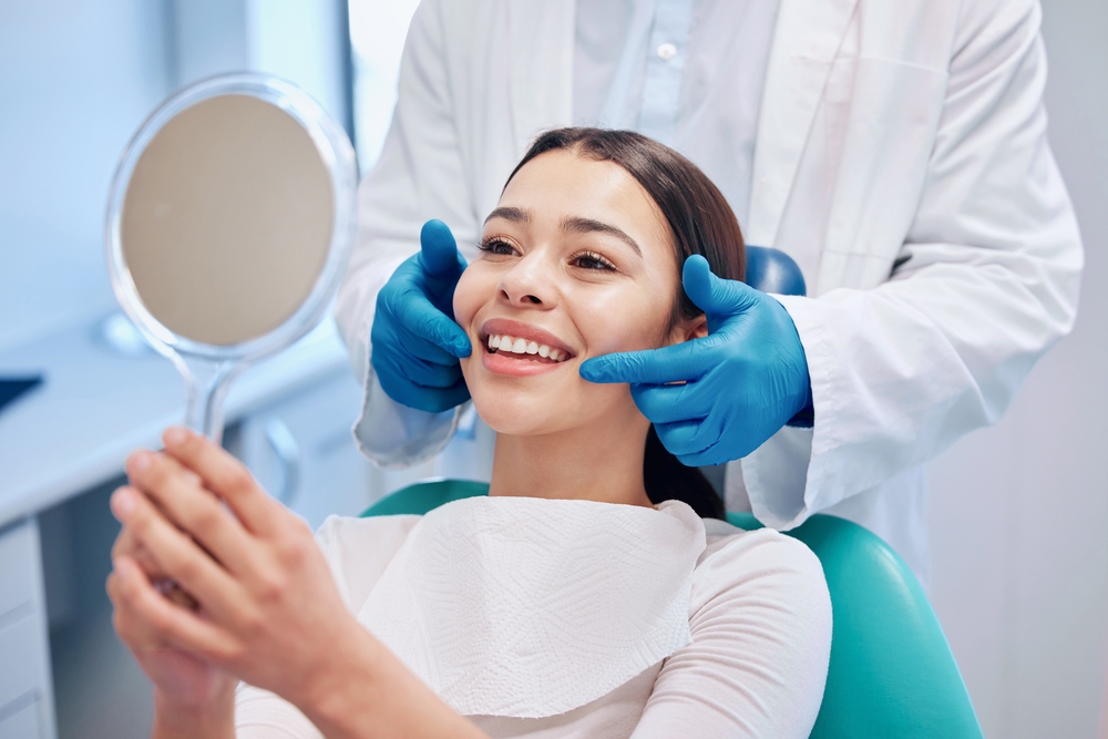 woman in dental chair looking at her teeth in a mirror